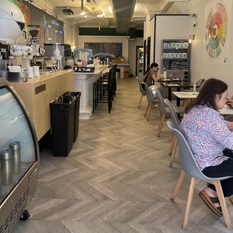 Interior of Botbar Vegan Cafe with a robot barista, bar seating, and customers at tables.