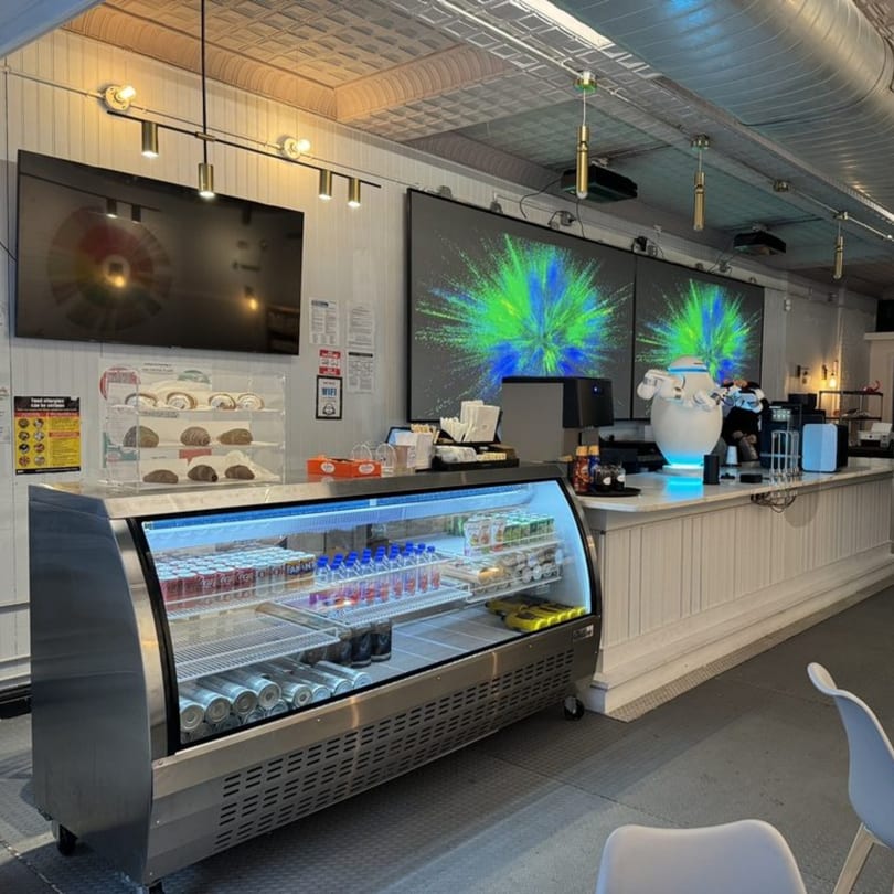 Interior of Botbar Vegan Cafe with a display case, counter, and large screens showing abstract art.