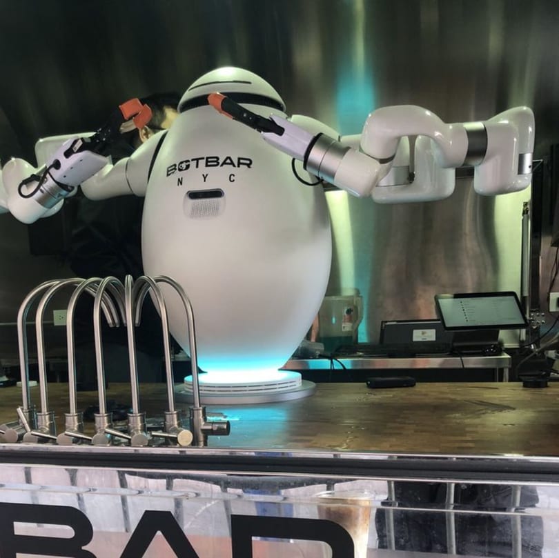 A large white robot with the "Botbar NYC" logo stands behind a counter with drink dispensers.